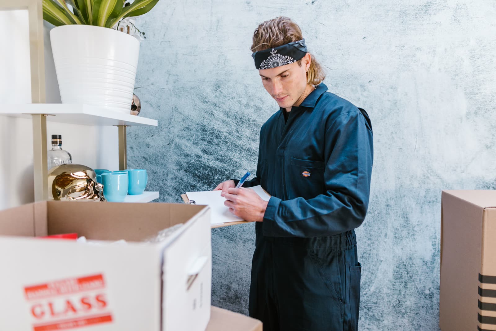 A remover checking an inventory list on a clipboard beside packed boxes