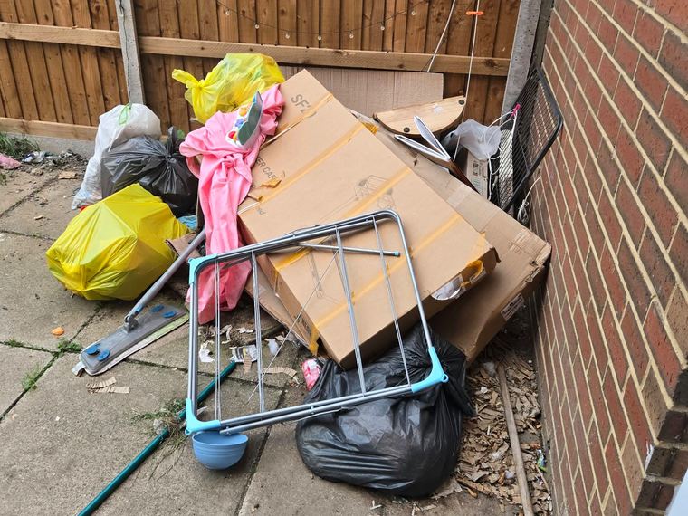 Boxes, bin bags and a broken clothes airer piled in the corner of a back garden before clearance