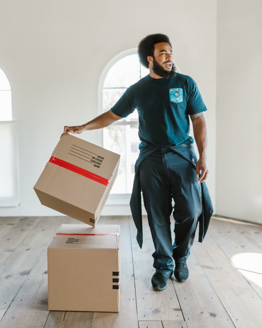 A remover carrying a taped cardboard box into an empty living room