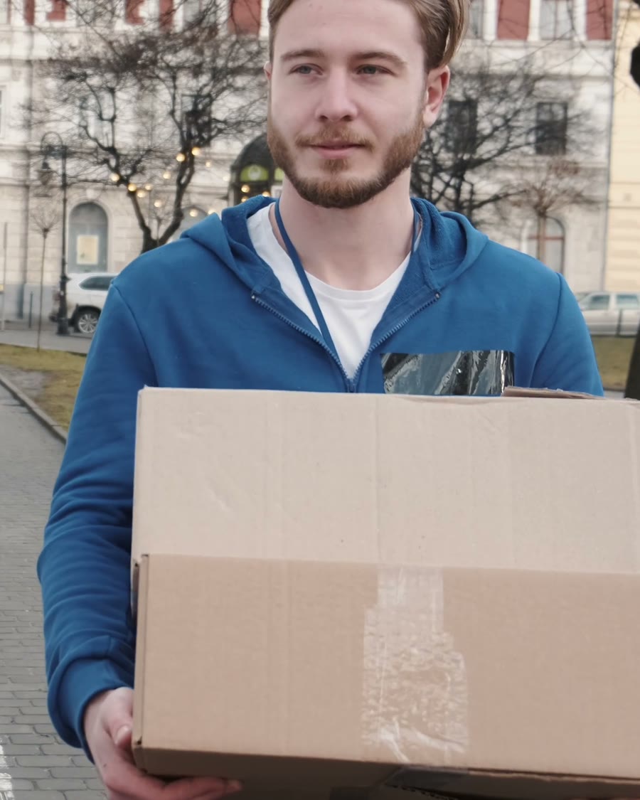 A remover carrying a taped cardboard box from a van to a front door